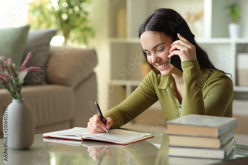 Fotografie Happy young woman talking on phone and checking agenda