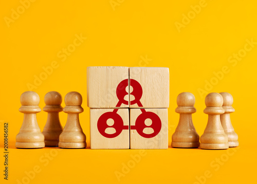 Wooden blocks showing a network connecting people, surrounded by pawns on yellow background