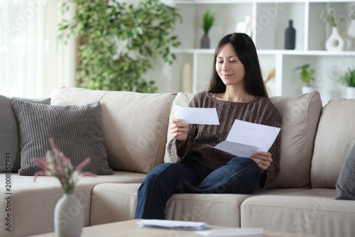 Satisfied asian woman reading letter on a couch at home
