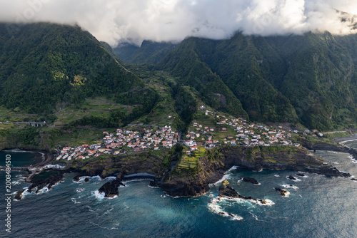 Seixal coastline with residential area, terraced hillsides, and rugged volcanic rocks. Atlantic coast of Madeira Island at sunset