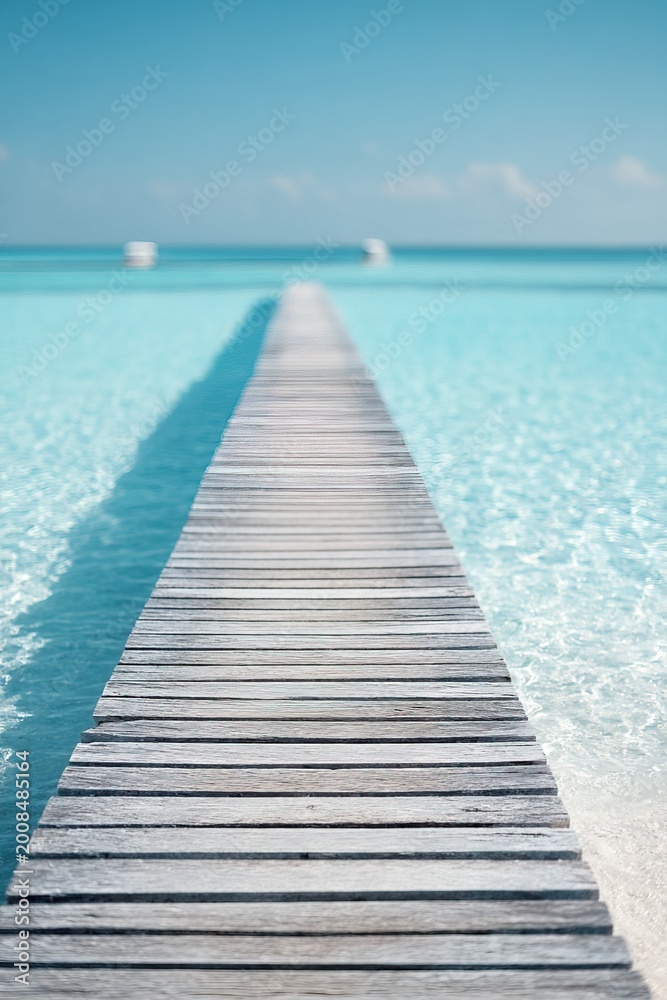Fototapeta premium A long wooden pier goes out over the clear blue water in resort. Visitors can walk along the pier to enjoy views of the ocean and boats. This spot attracts many tourists each year