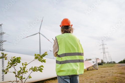 Engineer with reflective jacket standing near turbine blade at field