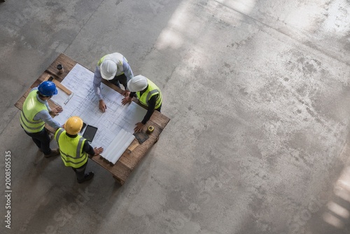 Top Down High Angle View of Four Construction Professionals Reviewing Blueprints on Site - Project Management and Architectural Planning Concept with Copy Space on Concrete Floor