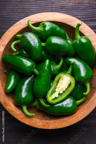 Wooden bowl filled with jalapeno peppers on dark table close view. Fresh green chili composition rustic food background