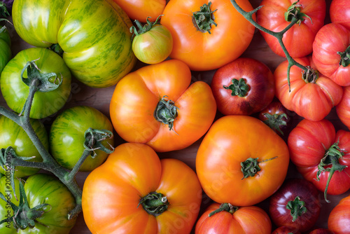 Assorted red, orange and green heirloom tomatoes tightly arranged. Colorful organic harvest, vibrant farm produce background