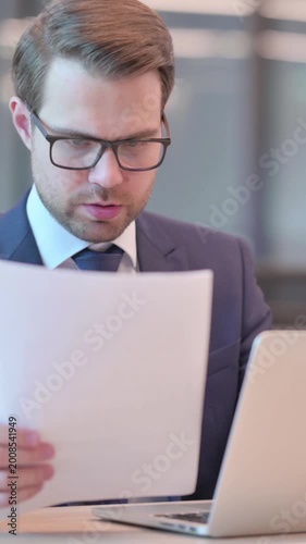Businessman with Laptop Reading Documents in Office