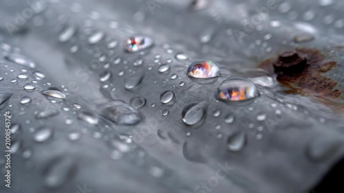 close up of water droplets on weathered corrugated metal featuring reflections of colorful lights and a rusty bolt symbolizing nature and decay with a macro perspective