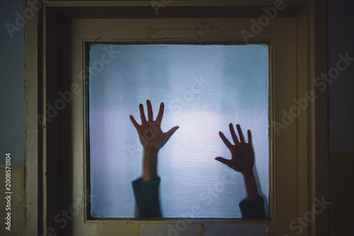 Shadow of woman’s hands on frosted glass descending slowly, suspenseful crime concept with trapped victim mood