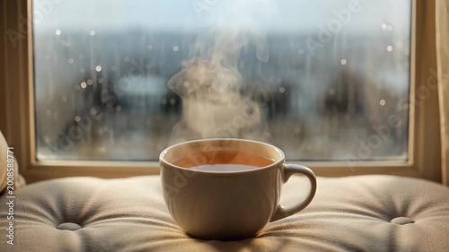 Steaming hot cup of tea on a rainy window sill cozy atmosphere.