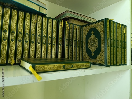 Collection of green Holy Quran books with gold ornaments on a white shelf