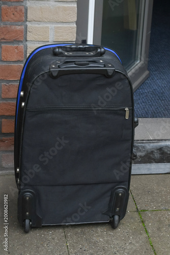 Black suitcase placed at the entrance of a building on a cloudy day in an urban setting