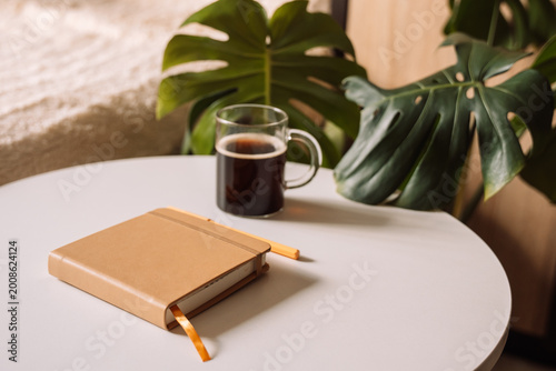 Closed notebook with pen and coffee on round white table.