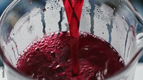 Crimson cranberry juice pours into a frosted glass pitcher, creating a refreshing beverage