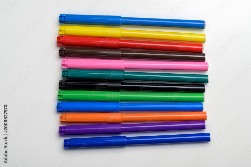 Fototapeta premium Top view of a collection of vibrant felt-tip pens in various colors neatly arranged horizontally on a white surface. Perfect for art, education, and creative design project concepts