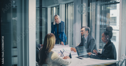 Business Manager Leads a Focused Planning Meeting in a Glass Office, Guiding a Diverse Team as They Review Reports, Discuss Strategy, Analyze Performance Metrics, Share Ideas