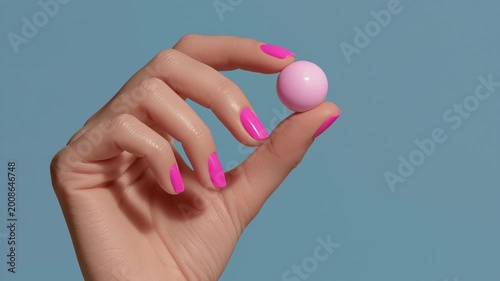 Female hand with bright pink nails holds a glossy pink ball against a soft blue background, showcasing a close-up view of the hand's delicate grip and the ball's shine