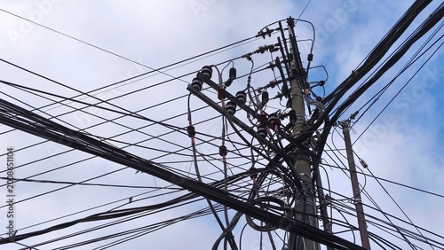 Complex network of power lines and utility pole against cloudy blue sky. Intricate electrical infrastructure. High voltage wires