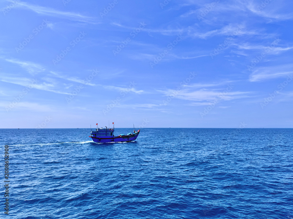 Obraz premium Distant view of a blue vessel cruising on the wide blue ocean