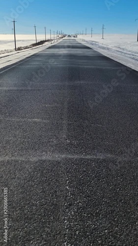 Powerful gusts of wind swirl snowflakes over an empty asphalt road. The contrast between the dark pavement and white snow creates a stunning visual, showcasing winter's magic. Vertical 4K footage.