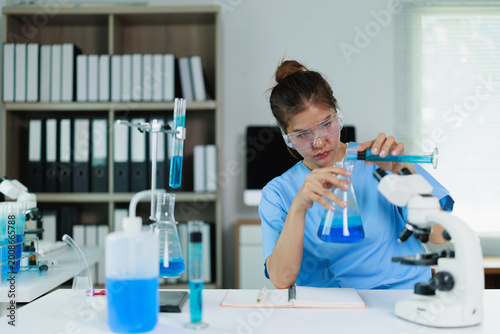 Cuadro en lienzo Woman scientist in protective glasses performing chemistry experiment with blue