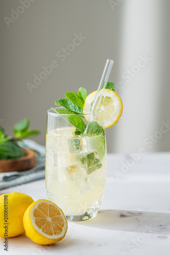 A refreshing summer drink with lemon, mint, and ice in a glass on a light background.