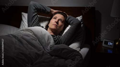 Woman unable to sleep, lying in bed with her hands behind her head, awake in the darkness. Insomnia and anxiety concept.