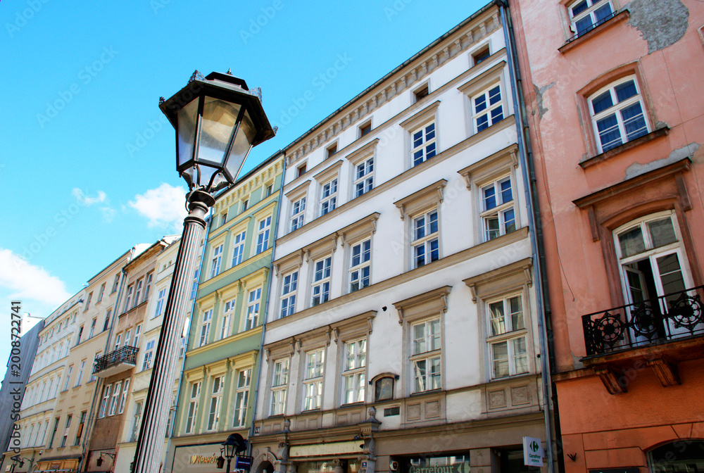 Obraz premium Colorful historic townhouse line a charming street in Krakow old town under a bright blue sky. Classic European street lamp in the foreground. Old street flats. 