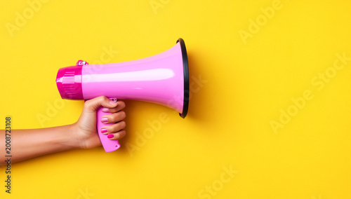 hand holding bright pink megaphone against vibrant yellow background for communication and promotion