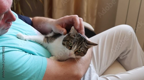 A middle-aged man relaxes in an armchair, tenderly holding a cat in his arms, exuding calm and affection