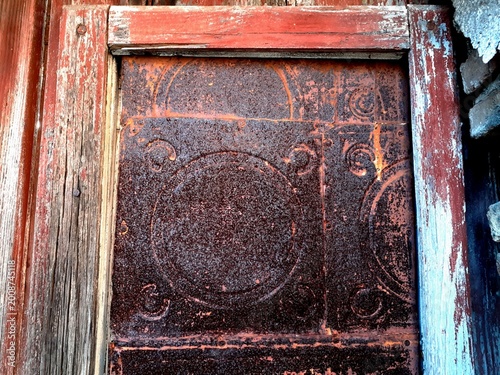 Dettaglio di una vecchia e abbandonata porta in legno dipinto di rosso con pannelli di ferro arrugginito.