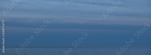 Bilde på lerret Peaceful coastal scene with gentle waves washing onto the shore and cliffs rising in the distance under a soft dusk sky