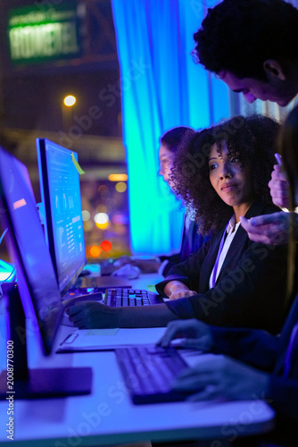 Fotografie Focused African American female cybersecurity expert looking up while discussing threat intelligence in a neon glowing SOC