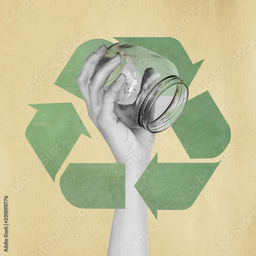 Hand holding an empty glass jar against a green recycling symbol on a textured background