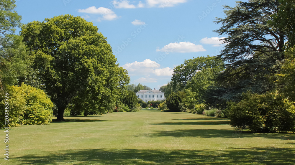 Fototapeta premium Historic white house standing at end of expansive green lawn, surrounded by lush trees under a summer blue sky