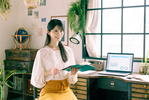 Fotografija 自宅の部屋でデスクの前に座って手帳を持って微笑む若い日本人女性