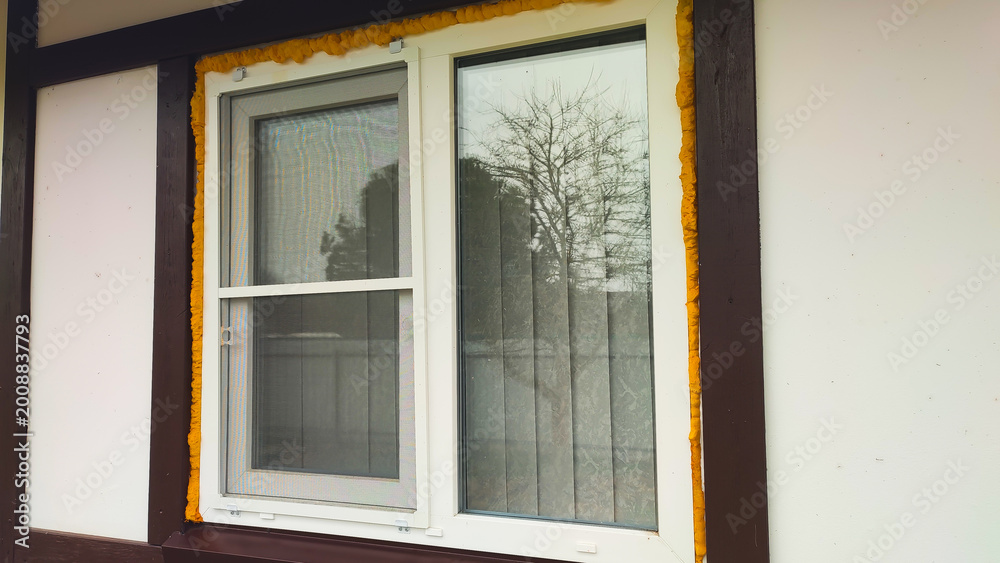 Fototapeta premium The window shows a yellow trim with clear glass reflecting trees outside.