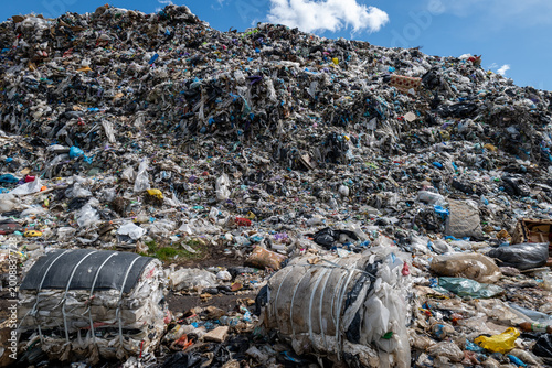 Workers and machines gather waste at a municipal trash site filled with heaps of garbage under a blue sky