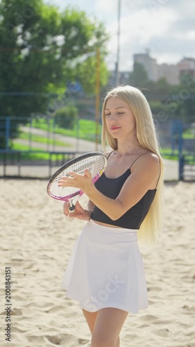 Young woman adjusts grip of tennis racquet and prepares for her next shot. Female enjoying sunny day on court. Player poses gracefully on bright sunny day. Portrait of young female player. 4K, UHD