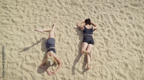 Two females training on bright day at sandy beach. They perform various exercises while enjoying the warm sun and beautiful surroundings. Female stretching during sunny morning. Healthy lifestyle