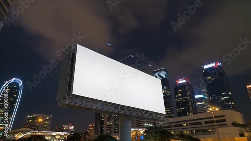 A large blank billboard stands prominently in a cityscape at night
