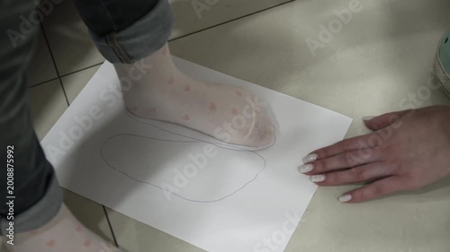 Close up of a person's foot wearing socks being traced with a blue pen onto a white piece of paper by another individual for accurate size measurement or orthopedic purposes.