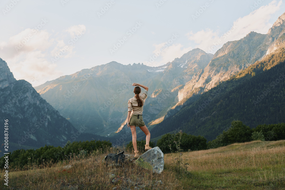 Fototapeta premium Woman outdoors in casual attire, enjoying a mountain landscape, daylight sun highlights vibrant nature, wide scenic terrain, relaxed lifestyle moment amid rugged slopes