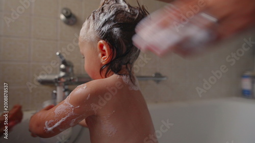 Foto Mother styling toddler’s wet hair into playful punk shape with shampoo foam duri