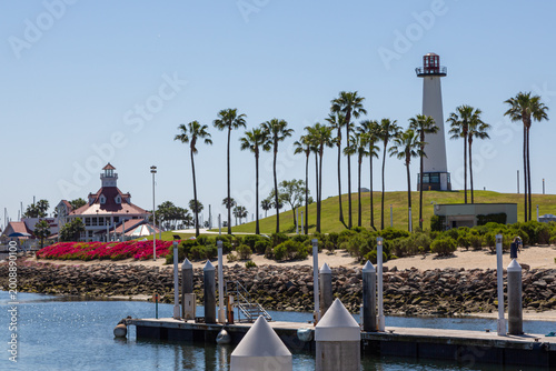 Shoreline Park lighthouse in San Diego with palm trees and blue sky. Marina harbor with pier and calm sea water. Lighthouse at Shoreline Park in San Diego near marina harbor. Coastal harbor with