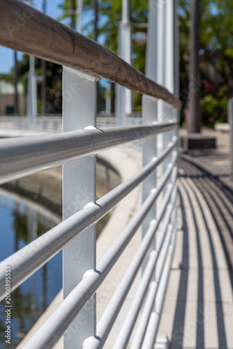 Metal railing along waterfront walkway with perspective lines and shadows. Urban promenade with shallow depth of field. Close view of metal railing on waterfront path with leading lines and shadows