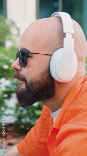 Happy bearded man in casual clothes and white casual headphone riding bicycle at urban street. Professional young male going to work on bicycle in city street. Slow motion.
