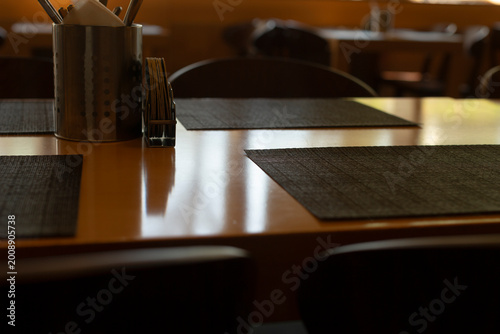 Tableau sur toile Late afternoon placemats on wooden table with warm window light, staff aligning
