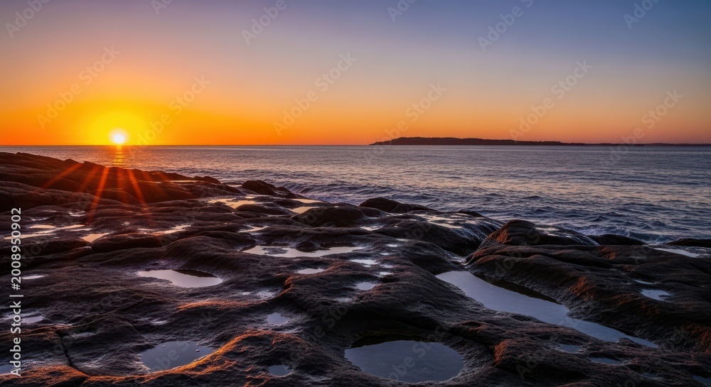 Naklejka premium Stunning sunset over a rocky coastline with tide pools and calm ocean