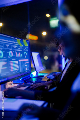 Картината върху платно IT specialists and data analysts monitoring real-time cybersecurity dashboards and network metrics in a high-tech operations center at night