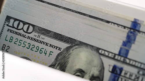 Stack of 100 dollar bills being processed by electronic money counter. Banking automation for financial literacy and cash savings protection. Detail currency bills and digital display during financial